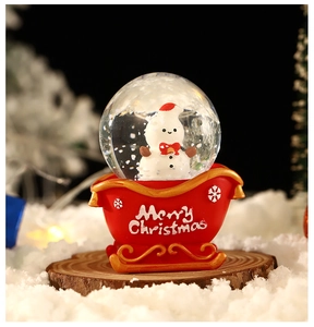 Detail of a Christmas snow globe featuring a snowman in a red sleigh base with gold accents