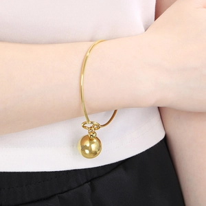 Minimalist gold knot bracelet featuring a smooth hollow sphere pendant on a model wrist