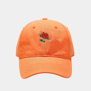 Dettaglio di un cappellino in cotone arancione con ricamo a rosa rossa e finiture curate
