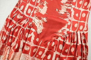 Detail of red and cream artistic print on pleated A-line dress with smooth stitching