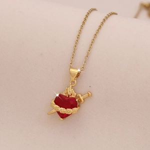 Vue macro du pendentif sacré cœur doré avec pierre rouge et épée sur tissu beige doux