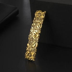 Detailed close-up of a vintage golden rectangle hair clip with embossed floral carvings