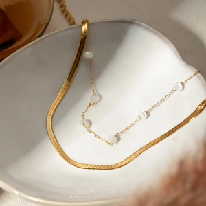 Detailed shot of double-layer 18K gold snake chain with white beads in a jewelry dish
