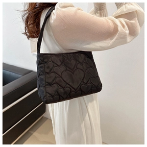 Détail d'un sac à bandoulière noir matelassé en forme de cœur porté par un mannequin
