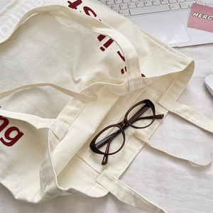 Vue à plat d'un sac cabas en toile avec lettres imprimées contenant lunettes et accessoires