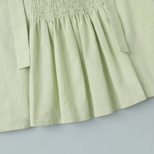 Detailed view of pale green cotton vest with elastic smocked waist and ruffled hem
