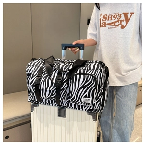 Large capacity zebra print duffel bag displayed on top of a white trolley suitcase.