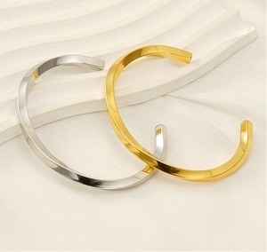 Close-up of gold and silver twisted C-shape stainless steel bracelets on white silk