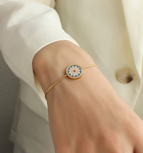 Detailed macro of gold snake chain bracelet with white daisy enamel flower charm