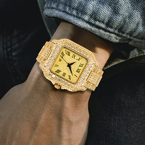 Close-up of gold iced-out square watch with Roman numerals on a denim jacket background