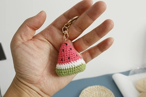 Macro detail of a handmade crochet watermelon keychain with golden metal clasp accessory