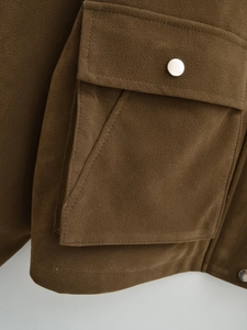 Nahaufnahme der braunen Wildlederjacke mit silbernem Druckknopf und feiner Naht