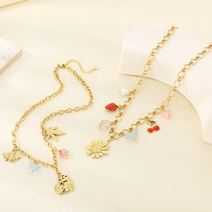 Gold stainless steel chain necklaces with daisy, heart, and bee charms on a stone display