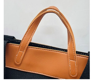 Detail of black canvas tote with brown leather handle and white contrast stitching