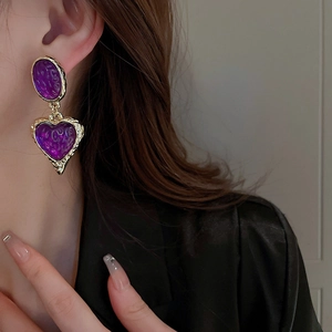 Retro purple resin heart drop earrings with gold trim worn by a model in soft light
