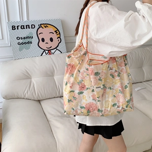 Close-up of floral tote bag with bright orange trim and woven shoulder strap