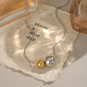 Detailed view of silver snake chain with gold and silver ball pendants on aesthetic paper