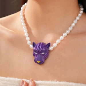 Gros plan d'un pendentif tête de léopard violet sur un collier de perles blanches
