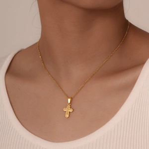 Detail view of a vintage gold cross pendant necklace worn by a model on ribbed top