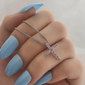 Detail of silver cross pendant with pink cubic zirconia stones held between fingers