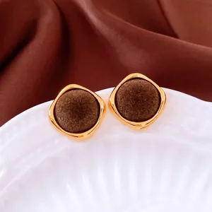 Retro gold square earrings with brown flocking detail on a textured white porcelain plate