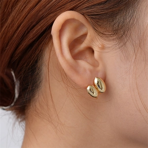 Close-up of elegant gold double bean geometric earrings worn on ear with polished finish
