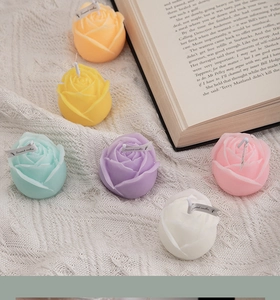 Top view of multicolored rose-shaped scented candles on a white knit cloth with a book
