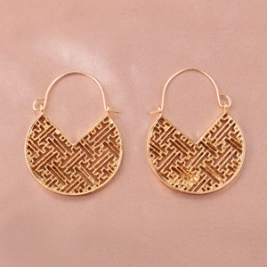 Close-up of golden hollow geometric fan earrings on a soft pink satin fabric