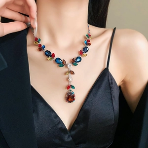 Close-up of a silver necklace featuring vibrant colorful zircon leaves and a red teardrop pendant