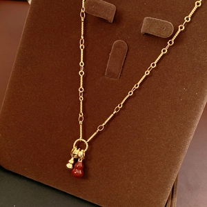 Detail of 18k gold plated red gourd necklace displayed on a brown velvet stand