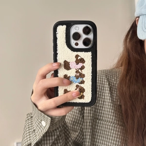 Close-up of plush bear embroidery on a beige iPhone case held by a person