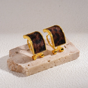 Close-up of leopard print faux fur earrings with gold metal trim on a stone