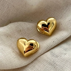 Detailed close-up of polished gold heart stud earrings on a textured linen background