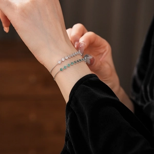 Detailed view of silver clover bracelets with white and green zircons on a model's wrist