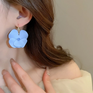 Detailed view of matte blue flower earrings with gold hooks worn by a model