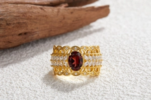 Macro shot of gold hollow ring with red oval gemstone and clear accents on wood