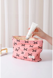 Action shot of putting hand cream into pink cotton makeup bag with black bow patterns