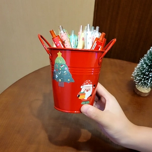 Red Christmas metal pen holder with cartoon Santa stickers on a wooden desk