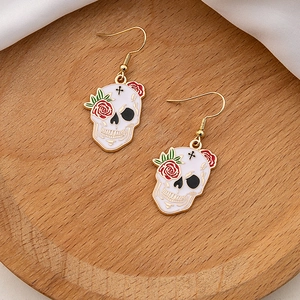 Detail of skull earrings with red roses on a wooden tray with white silk fabric decor