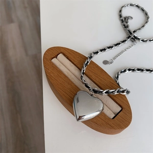 Silver heart pendant necklace with black leather woven chain on a wooden display stand