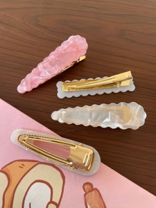 Detail of four acetate hair clips with pink marble texture on a dark wood background