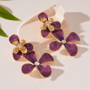 Detail view of purple floral earrings with gold edges and crystal center on stone
