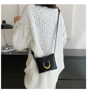 Detail of a chic black leather crossbody bag with a distinctive golden horseshoe clasp