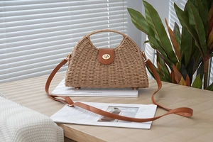 Detail of woven straw bag showing brown leather flap, gold metal twist lock and texture