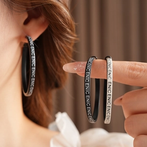 Détail de boucles d'oreilles circulaires en cuir avec motif NICENICENICE répété en noir