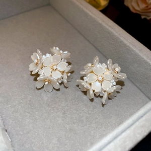 Macro shot of white floral cluster stud earrings with pearlescent petals and golden beads