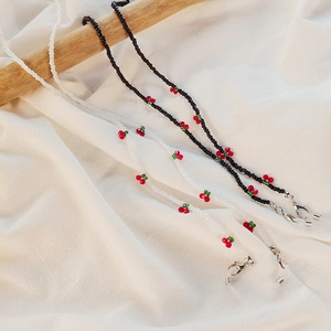Detail of beaded glasses chain with red cherries and lobster clasp on wooden stand