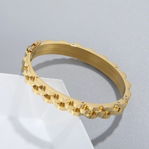 Détail d'un bracelet en acier doré avec bords festonnés et finition texturée élégante