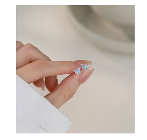 Close-up of mini light blue butterfly stud earrings held between fingers for scale
