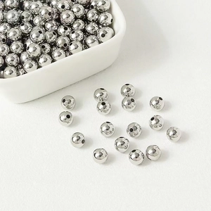 Polished silver metal round beads for jewelry making displayed in a white bowl